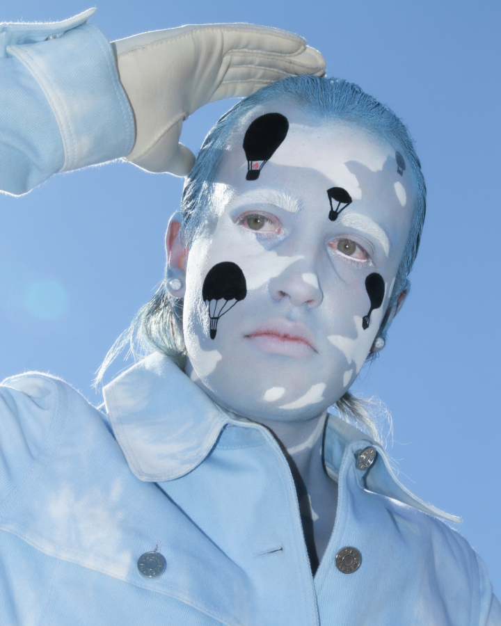 Jesse Clark posing blue and white cloud facepaint on against a sky blue background.
